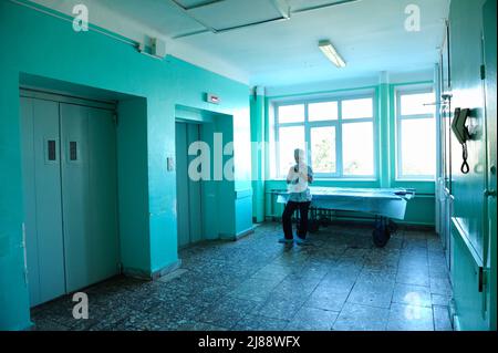 Ärztin in einem blauen Laborkittel, die im Flur des Krankenhauses steht und auf einen Aufzug wartet, eine Trage. 12. Januar 2019. Kiewer Regionalklinik Stockfoto