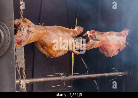 Prozess des Kochens von Widderkadavern am Spieß auf dem sommerlichen Lebensmittelmarkt: Nahaufnahme Stockfoto