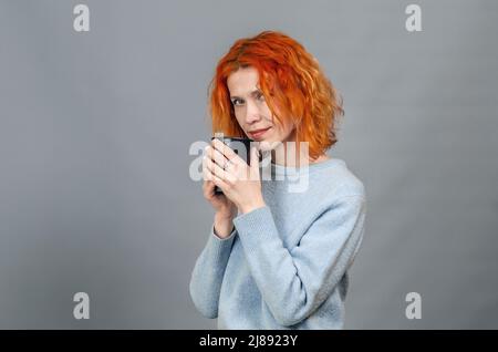 Porträt einer niedlichen rothaarigen Frau in legerer Kleidung mit Getränk in den Händen. Blick auf die Kamera. Stockfoto