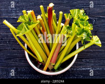 Junge saftige Rhabarberstiele stehen auf einem Holztisch in einer Metallschale. Frische saftige vegetarische Bio-Lebensmittel. Stockfoto