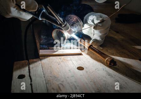 Die Hände des Schweißers in Handschuhen. Reparatur von Kaffee türk durch Schweißen. Nahaufnahme Stockfoto