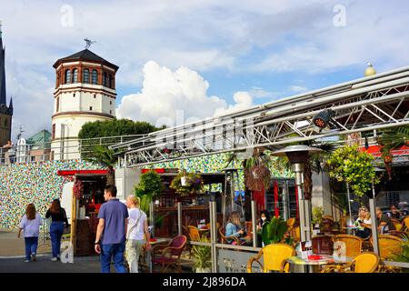 Die beliebte Touristenattraktion Rheinpromenade in Düsseldorf/Deutschland mit Outdoor-Restaurant und historischem Burgturm im Hintergrund. Stockfoto