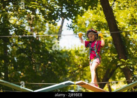 Das konzentrierte Mädchen überwindet sorgfältig Hindernisse im Seilpark Stockfoto