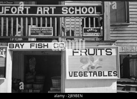 Obstschild. Beaufort, South Carolina. [Schilder: 'Beaufort Art School;. General Lafayette sprach von dieser Veranda 1824; Public stenographer; Bay Fish Co; Obst - Gemüse'. 1824 machte der französische Marquis de Lafayette, der letzte überlebende Generalmajor des amerikanischen Revolutionskrieges, eine Tournee durch die 24 Staaten der Vereinigten Staaten. Er hielt eine Rede vom Balkon des John Mark Verdier House, auch bekannt als Lafayette Building]. Stockfoto