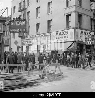 Salvation Army, San Francisco, Kalifornien. Allgemeine Sicht auf Armee und Menschenmengen. [Schilder: „Danger - Street Closed; Steam Welcome here; Headquarters for Union Men - We Sell Everything Men Wear; Can't Bust 'EM Work Clothing; Max's Shop for Men - Famous for Gloves“]. Stockfoto