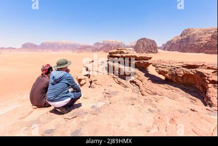 Ein Tourist mit seinem ortskundigen Fremdenführer, der den Steinbogen in der Wüste von wadi Rum in Jordanien betrachtet. Blauer Himmel Stockfoto