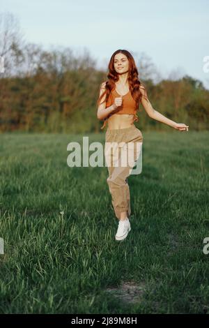 Eine Frau arbeitet und rennt mit einem Lächeln und guter Laune durch das Feld im Park und blickt auf die wunderschöne Sommernatur um sie herum Stockfoto