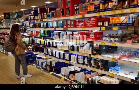 Frau, die mit einem Korb im Haushaltswarengang des Aldi Supermarkts, Großbritannien, einkauft Stockfoto