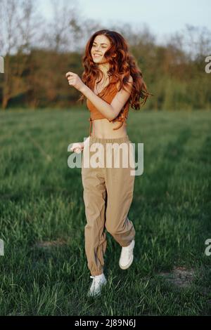 Eine Frau arbeitet und rennt mit einem Lächeln und guter Laune durch das Feld im Park und blickt auf die wunderschöne Sommernatur um sie herum Stockfoto