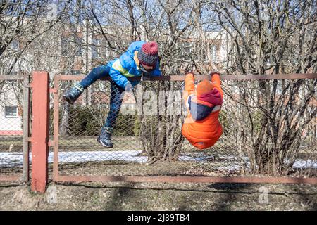 Zwei Kinder klettern über den Zaun. .Spiele für Kinder. Stockfoto