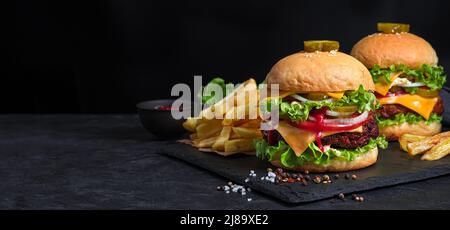 Zwei Burger, Pommes Frites und Saft auf schwarzem Hintergrund. Stockfoto