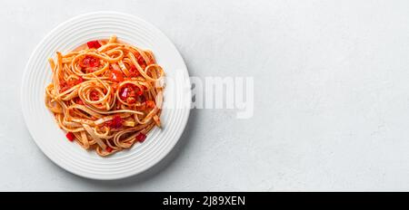 Frische traditionelle italienische Pasta mit Linguini mit Tomatensauce auf grauem Hintergrund. Stockfoto