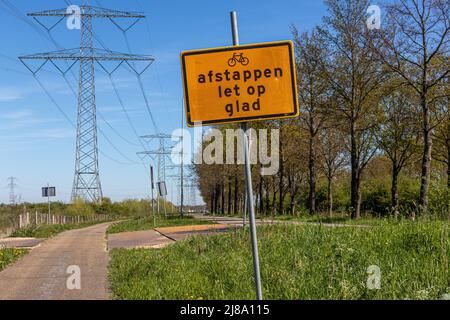 Metallschild mit der niederländischen Aufschrift Afstappen, Lass dich, froh, was bedeutet, beim Aussteigen, aufpassen, rutschig. Ciclovia, Landstraße, Bäume und Hi Stockfoto