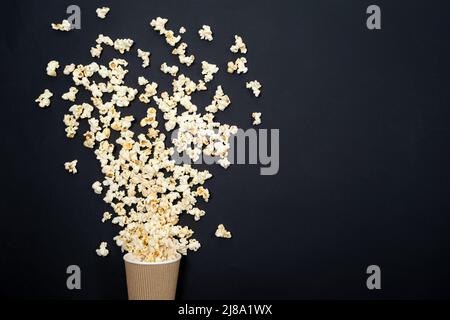 Popcorn wird aus dem Glas auf einem schwarzen Hintergrund, von oben betrachtet, ausgestreut. Ein Spritzer Popcorn Stockfoto