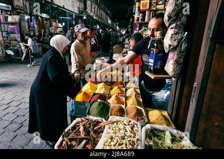 Damaskus, Syrien - Mai 2022: Älteres Paar kauft Lebensmittel, Kräuterpflanzen und Gewürze auf dem Suq Al Hamidiyah Straßenmarkt in Damaskus Stockfoto