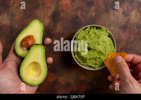 Traditionelle lateinamerikanische mexikanische Sauce Guacamole in Tonschüssel, schneiden Sie halbe Avocado- und Avocado-Sandwiches auf dunklem Hintergrund. Draufsicht Stockfoto