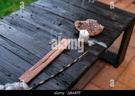 Ein Holztisch im Freien mit Räucherstäbchenhalter, Stab, Kerze und spirituellen Kristallen, die ein kraftvolles Ambiente schaffen Stockfoto