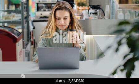 Vorderansicht kaukasisch beschäftigt fokussierte Frau Mädchen freiberuflicher Arbeiter Benutzer smm Spezialist Vermarkter arbeiten Laptop eingeben Kaffee in Café online trinken Stockfoto