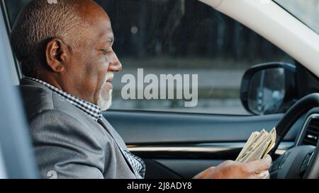 afroamerikanischer Geschäftsmann sitzt im Auto mit Haufen Dollar Zählen Papier Banknoten zählt Geld Bargeldzahlungen hohes Einkommen erfolgreich Stockfoto