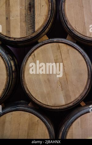Unbeschriftete Whiskey-Fässer aus amerikanischer Eiche, die mit Holzkeil im Lagerhaus der Brennerei aufeinander gestapelt wurden Stockfoto