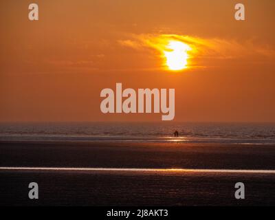 Ein Paar in der Ferne genießt den Sonnenuntergang an einem leeren Strand Stockfoto