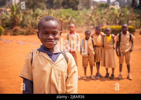 Afrikanischer Schuljunge mit Down-Syndrom auf dem Schulhof mit seinen Schulkameraden im Hintergrund unscharf Stockfoto