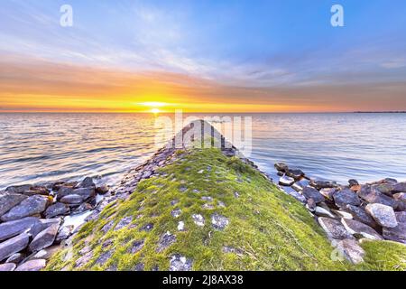 Typischer Bau von Basalt-Wellenbrechern am IJsselmeer in der Nähe der Stadt Hindeloopen in der Provinz Friesland bei Sonnenuntergang, Niederlande. Stockfoto