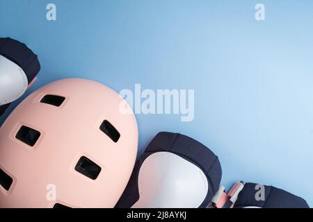 Draufsicht auf das Rollschuh-Schutzausrüstung-Set - Knie-, Ellbogen- und Handgelenkpolster sowie Helm in rosa Farben. Blauer Hintergrund flach lag Stockfoto