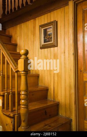 Eine Treppe aus Kiefernholz mit einem umgedrehten Neuholzpfosten in einem alten Haus im kanadischen Cottage-Stil aus dem Jahr 1850. Stockfoto