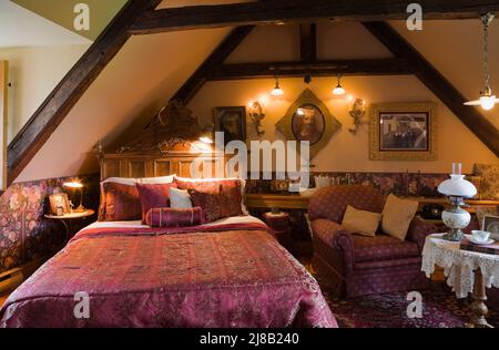 Queen-Size-Bett mit violettem Samt-Bettüberwurf im Hauptschlafzimmer im oberen Stockwerk im alten rekonstruierten Blockhaus im Stil von 1800s Canadian Cottage. Stockfoto