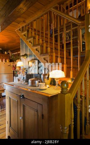 Antiker Holzschrank und eine Treppe aus Pinienholz in der Küche im alten rekonstruierten Blockhaus aus dem Jahr 1800s im kanadischen Cottage-Stil. Stockfoto