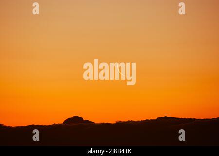 Schwindelender Mond am bunten Himmel. Satellit der Erde über der Stadt in Sonnenstrahlen. Astronomisches Phänomen. Heller Sonnenuntergang oder Sonnenaufgang. Stockfoto