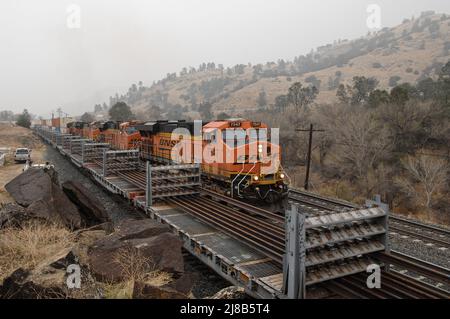 Die BNSF 7547 fährt einen Stapelzug hinauf zur Tehachapi-Schleife, während sie an mit neuen Schienen beladenen Schienenfahrzeugen vorbeifährt Stockfoto