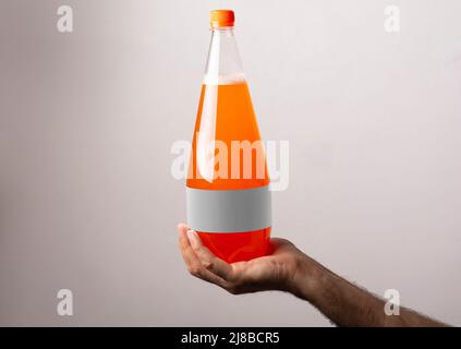 Orange Soda-Plastikflasche in männlicher Hand isoliert auf grauem Hintergrund, Modell-up-Serie Vorlage bereit für Ihr Design. Label-Auswahlpfad enthalten. Stockfoto