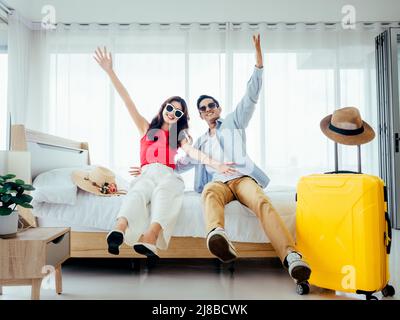 Bereit für die Reise, glücklicher Urlaub, Check-in. Konzept für Sommerferien. Asiatisches Paar, das mit Freude die Hände hebt, Mann und Frau tragen eine Sonnenbrille und lächeln glücklich Stockfoto