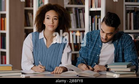 Zwei Studenten, junger Mann und Mädchen, die Hausaufgaben machen, sitzen am Schreibtisch in der Bibliothek und schreiben Notizen aufmerksam dem Dozenten beim Unterricht in der Klassenzimmer-Gruppe zu hören Stockfoto