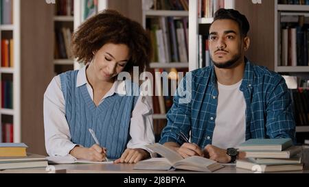 Zwei Studenten, junger Mann und Mädchen, die Hausaufgaben machen, sitzen am Schreibtisch in der Bibliothek und schreiben Notizen aufmerksam dem Dozenten beim Unterricht in der Klassenzimmer-Gruppe zu hören Stockfoto