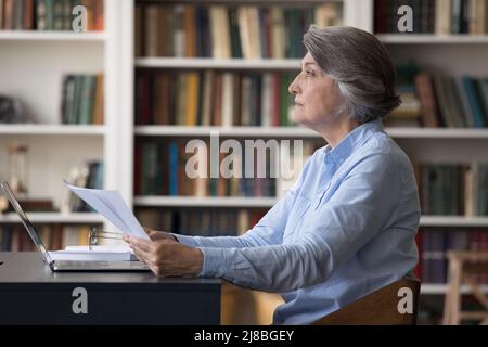 Seriöse, konzentrierte ältere Geschäftsfrau, die Papierdokumente analysiert Stockfoto