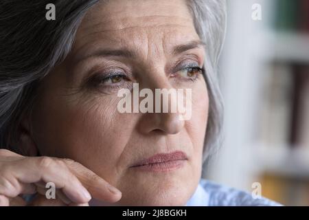 Nachdenkliche reife grauhaarige Dame, die in tiefem Denken wegschaut Stockfoto