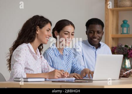 Eine vielfältige Gruppe von glücklichen Praktikanten und Mentoren, die am Laptop sprechen Stockfoto