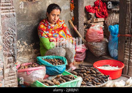 Kathmandu, Nepal - 27. Oktober 2021: Hindu-Frau verkauft getrockneten Fisch in den Straßen von Kathmandu. Frau in farbigen Kleidern wartet auf die Pudding Stockfoto