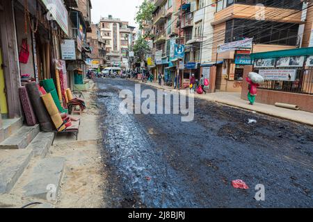 Kathmandu, Nepal - 27. Oktober 2021: Stadtbild der nepalesischen Hauptstadt. Eine ansonsten staubige Straße wird provisorisch mit Teer besprüht, um den Staub zu binden. Po Stockfoto