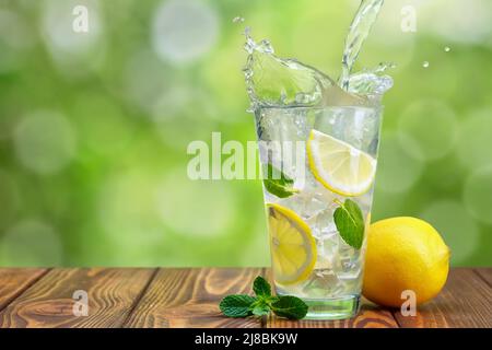 Limonade in Glas auf Holztisch mit grün verschwommenem Hintergrund Stockfoto