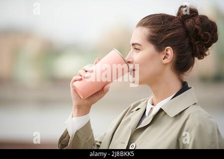 Seitenansicht der jungen Brünette Frau mit Haar Brötchen trinken aus Thermoskanne im Herbst Stockfoto