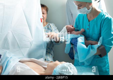 Krankenschwester hält neugeborenes Baby in der Nähe der Mutter im Krankenhaus Stockfoto