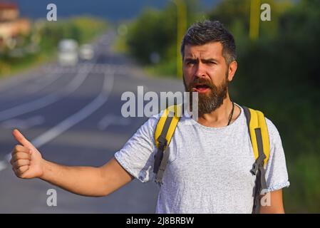 Auto-Stopp-Fahrt. Abenteuer- und Tourismuskonzept. Mann in legerer Kleidung winkt mit dem Auto und fährt am Straßenrand mit dem Anhalter. Reisen mit Autostop, mit Sommerausflug Stockfoto