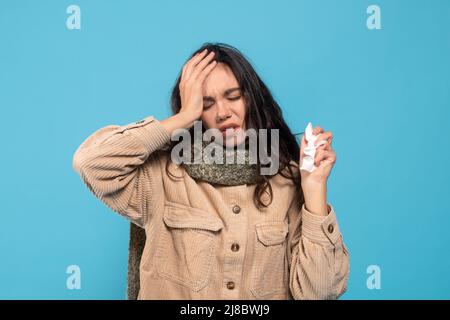 Unglückliche junge europäische Dame Brünette leidet an laufender Nase und Kopfschmerzen, hält Serviette, drückt Hand an Kopf Stockfoto