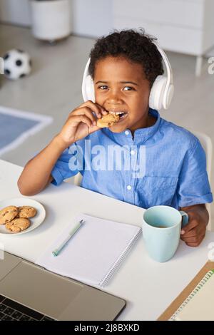 Porträt eines positiven schwarzen Schuljungen in kabellosen Kopfhörern, der während der Hausaufgaben eine Mittagspause macht Stockfoto