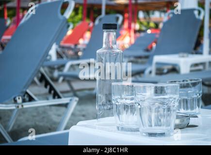 Ein kleiner ruhiger Touristenort Leptokarya in Griechenland. Leere Glaswasserflaschen und Trinkgläser auf einem Tisch in Griechenland. Stockfoto