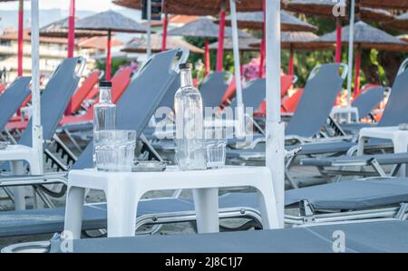 Ein kleiner ruhiger Touristenort Leptokarya in Griechenland. Leere Glaswasserflaschen und Trinkgläser auf einem Tisch in Griechenland. Stockfoto